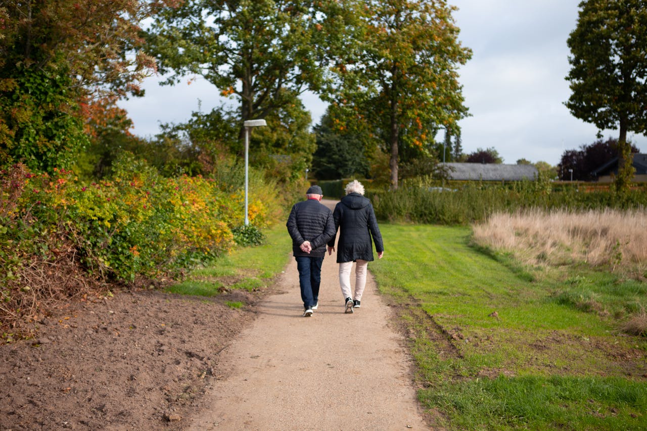 A couple walking down a scenic unpaved road surrounded by vibrant autumn foliage.